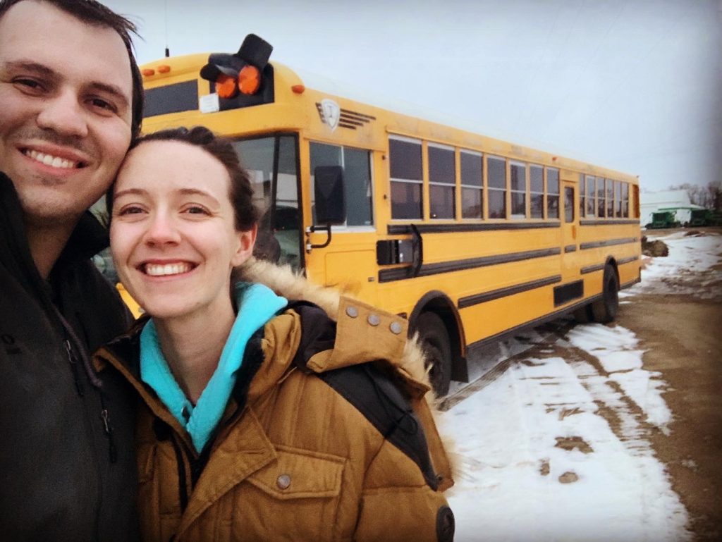 man and woman stand in front of a school bus