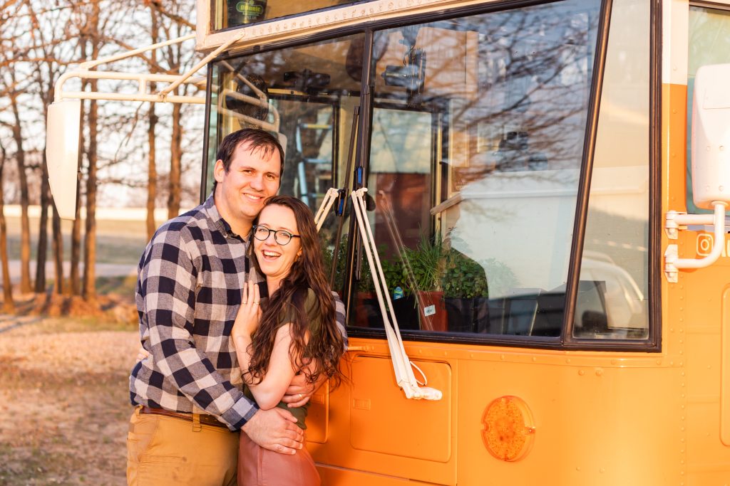husband and wife in front of an orange bus's windshield